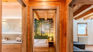 A wooden interior with a bed, nightstand, and a view of a forest through a window.