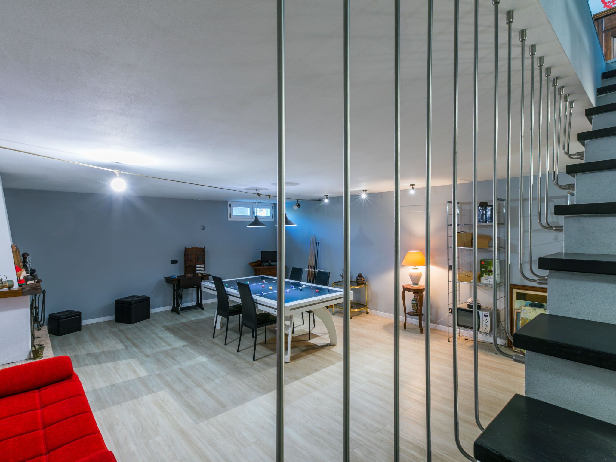 A modern living room with a pool table, a red sofa, and a staircase with metal railings.