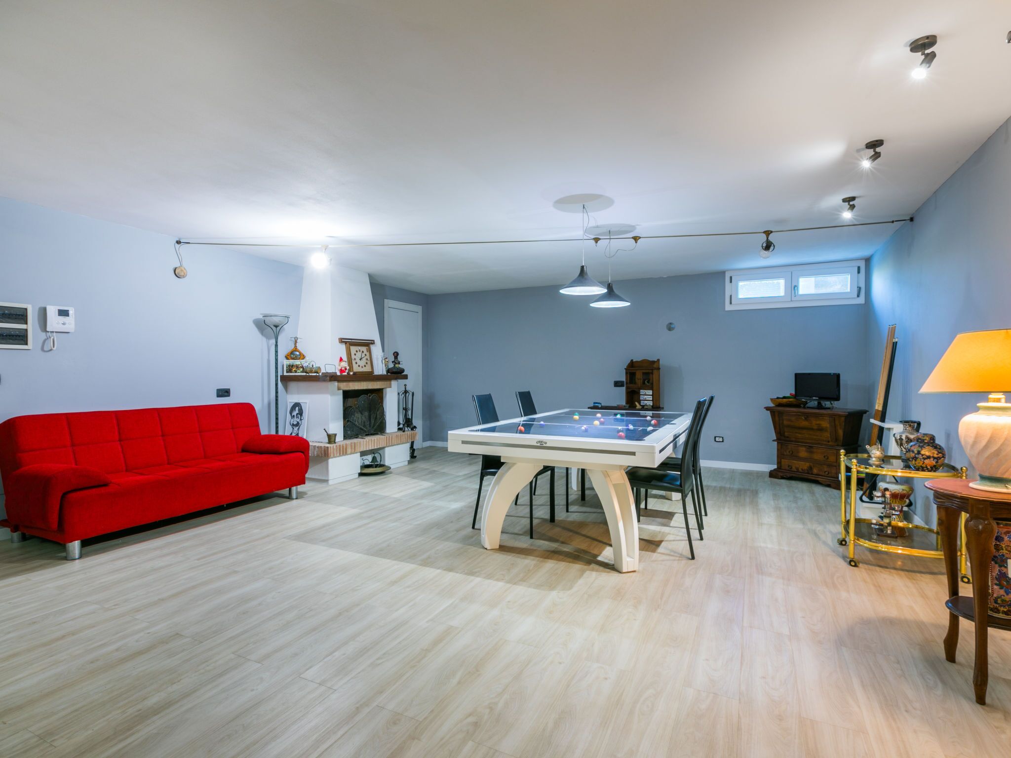 Un salón amplio con un sofá rojo, una mesa de futbolín y una chimenea.