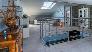 Un loft spacieux avec un plafond haut, une lucarne, une maquette de bateau en bois, un escalier avec une rampe en métal et un mur en pierre.