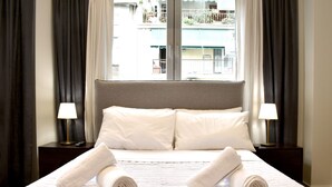 A hotel room with a large bed, two bedside lamps, and a view of a building through the window. - Siga-siga Luxury Acropolis Apt (Athens)