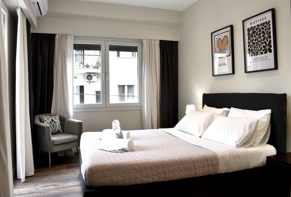 A hotel room with a bed, a chair, a window, and two framed pictures on the wall.