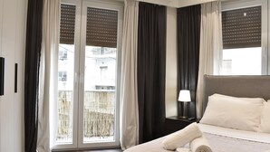 A hotel room with a bed, a nightstand, a lamp, and a view of the outside through a sliding door. - Siga-siga Luxury Acropolis Apt (Athens)