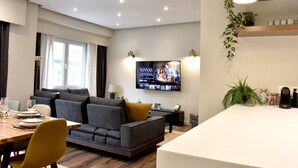 A modern living room with a sofa, dining table, and a TV mounted on the wall. - Siga-siga Luxury Acropolis Apt (Athens)