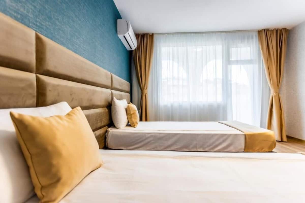 A hotel room with a large bed, beige bedding, a headboard, and a window with curtains.
