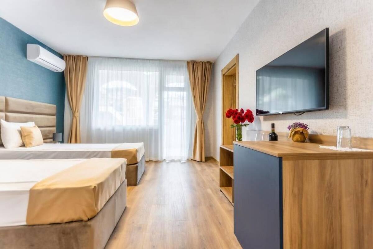 A hotel room with two beds, a TV, a desk, and a window with curtains.