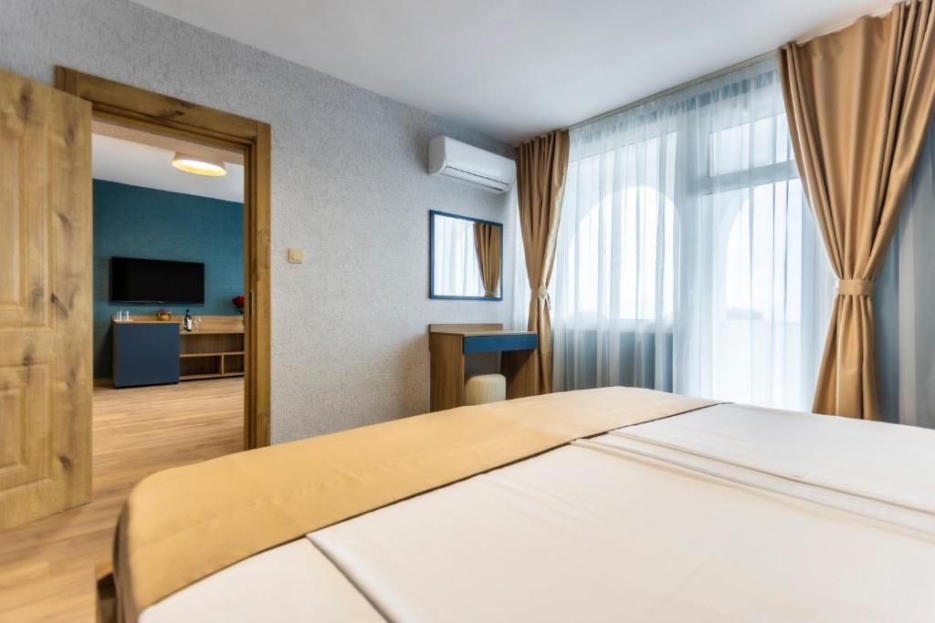 A hotel room with a large bed, a desk, a television, and a window with curtains.