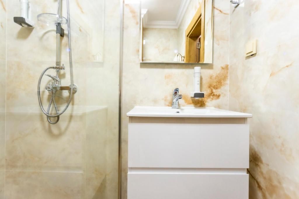 A bathroom with a glass-enclosed shower, a white sink, and a mirror above the sink.