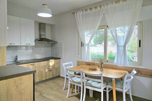 Enjoy meals in the compact kitchen with sink and stainless steel range hood, adjacent to a dining area with a wooden table and chairs.