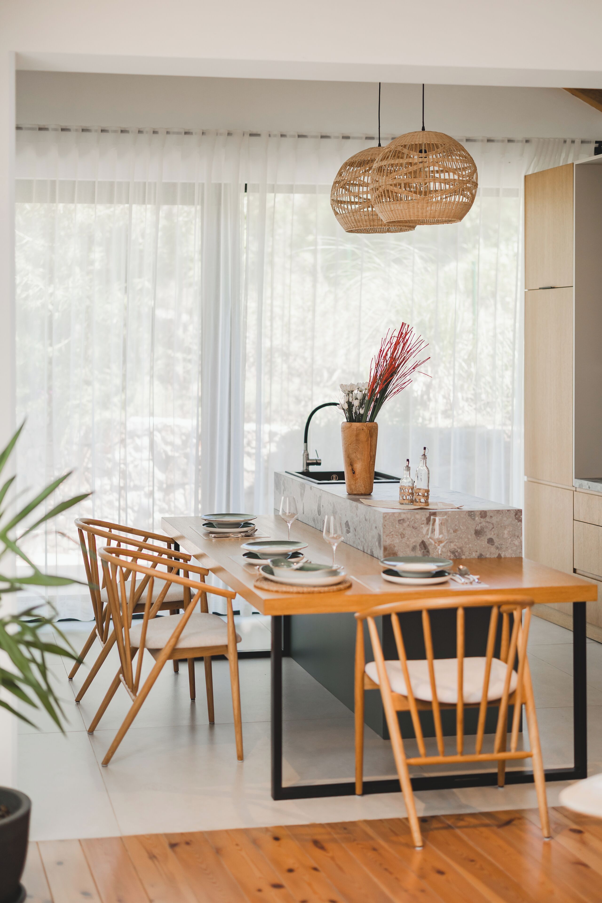 A modern kitchen with a wooden dining table, chairs, and a hanging light fixture.