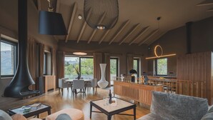 A modern living room with a fireplace, wooden furniture, and large windows offering a view of the outdoors. - Villa Diamonte - Ancient Stones, New Horizons (Đuraševići)