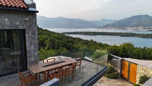 A balcony with a wooden table and chairs, overlooking a lake with mountains in the background. - Villa Diamonte - Ancient Stones, New Horizons (Đuraševići)