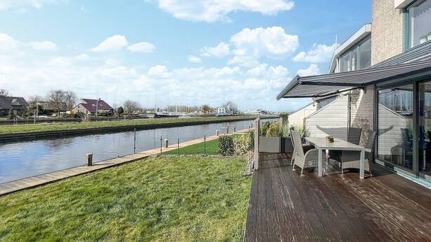 A riverside patio with a table and chairs, a wooden deck, and a view of a canal with boats. - Gorgeous home in Lemmer with WiFi (Lemmer)