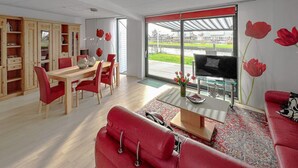 A modern living room with a red sofa, a dining table, and a TV. There is a large window with a view of a green landscape. - Gorgeous home in Lemmer with WiFi (Lemmer)