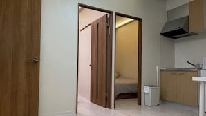 Um quarto com porta de madeira, uma cama, uma cozinha compacta e um lustre.