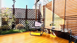 Um deck de madeira com mesa e cadeiras, cercado por um muro de madeira e vegetação.
