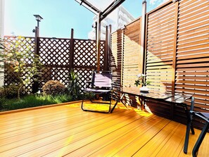 A wooden deck with a table and chairs, surrounded by a wooden fence and greenery.