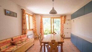 A dining area with a wooden table and chairs, a sofa, and a view through large windows. - L'Echaillon - Soldanelle (Névache)