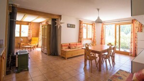 A spacious room with a wooden dining table, chairs, a sofa, and a large window providing natural light. - L'Echaillon - Soldanelle (Névache)