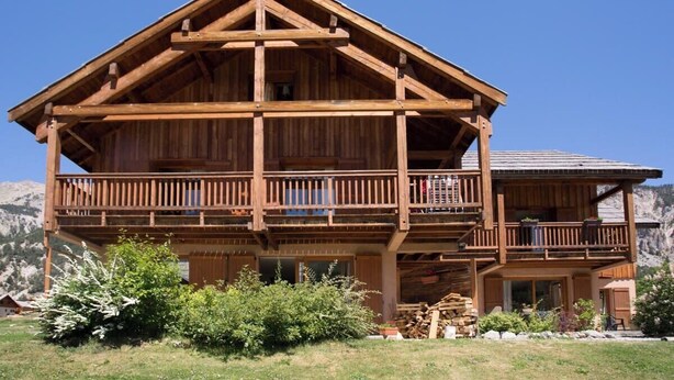 A wooden chalet with a balcony, a mountain backdrop, and a clear sky. - L'Echaillon - Soldanelle (Névache)