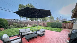 Een terras met een zwarte parasol, een bank en een tafel.
