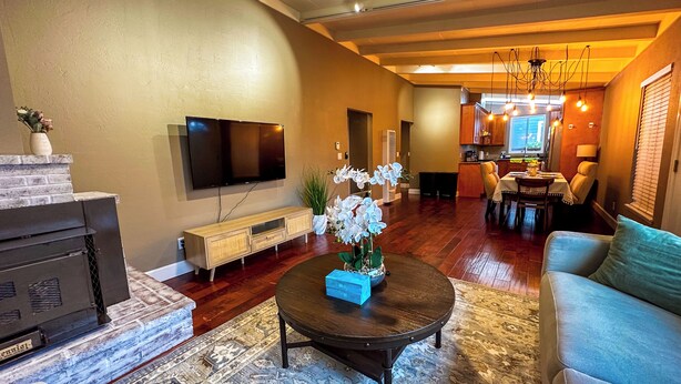 Een moderne woonkamer met een flatscreen televisie, een houten tv-meubel en een eethoek met een tafel en stoelen.