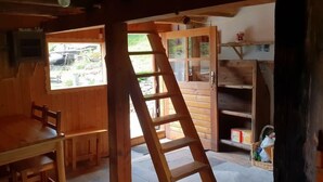 Ein Holzinterieur mit einem Esstisch, Stühlen, einer Himmelsleiter und einem Fenster mit Blick ins Freie.