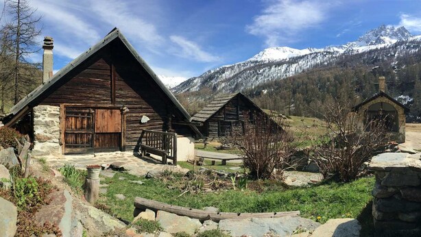 Ein rustikales Bergingeräte mit Steinunterbau und Holzwänden, vor der Kulisse schneebedeckter Berge.