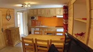 Une cuisine de taille réduite, dotée de meubles de rangement en bois, d’une table à manger et de chaises.
