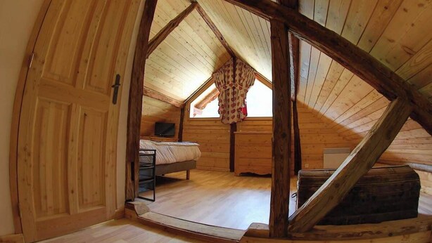 Une chambre mansardée en bois, avec un plafond en pente, un lit, une commode et un téléviseur.