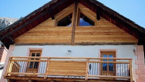 Un chalet en bois à deux étages, doté d’un balcon, d’un toit à deux versants et surplombant un paysage montagneux.