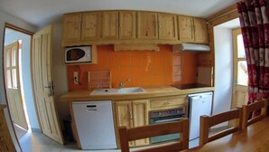 Une cuisine de taille réduite, dotée de meubles en bois, d’un four à micro-ondes, d’un évier et d’un lave-vaisselle.