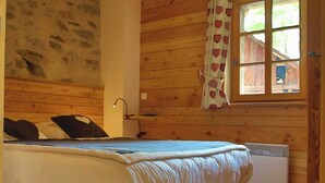 Ein Zimmer mit Holzwänden, einem Bett, einem Fenster mit herzenmuster Vorhängen und einem Wandheizgerät.