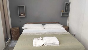 A neatly made bed with a green bedspread and white pillows, two bedside tables with small shelves, and a wicker basket on the floor. - GREEN ART STUDIOS (Roma)