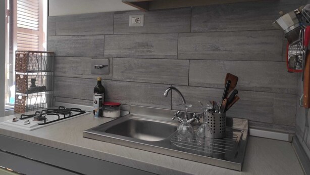 A modern kitchen with a stainless steel sink, gas stove, and a wine bottle on the counter. - GREEN ART STUDIOS (Roma)