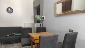 A small, compact living space with a wooden table and four grey upholstered chairs. A dark green sofa is positioned against the wall, and a globe is mounted on the wall above the sofa. - GREEN ART STUDIOS (Roma)