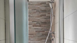 A shower area with a stone wall backdrop and a glass door. - GREEN ART STUDIOS (Roma)