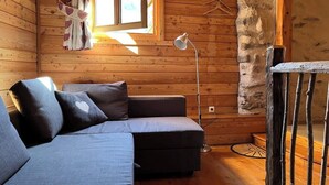 Interior acolhedor de uma cabana, com um sofá, um abajur e uma janela com cortinas.