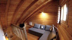 Uma cabana de madeira acolhedora com um quarto no estilo loft, incluindo um sofá-cama, uma escrivaninha e uma janela com cortinas.