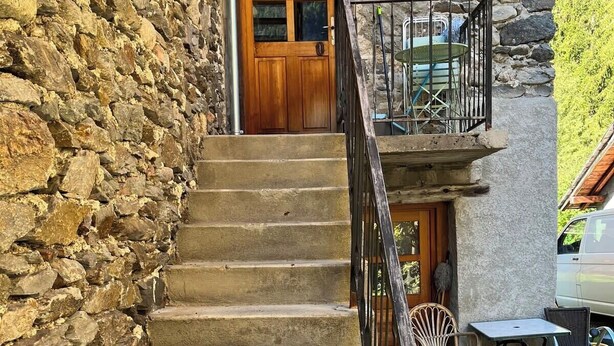 Escadaria de pedra que leva a uma porta de madeira, com área de estar ao ar livre e um carro estacionado perto.