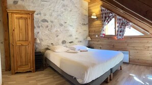 Quarto com parede de pedra, teto de madeira e cama com almofadas e cobertor.