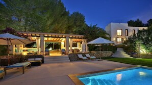Zona junto a la piscina con sillas de descanso, una pérgola y un muro de piedra.