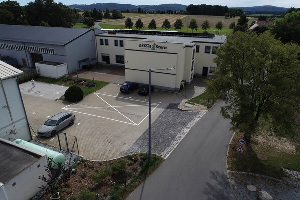 A building with a sign for 'Dreistern Resort Stern' indicating a pension facility. There is a parking area with marked spaces and a few cars.