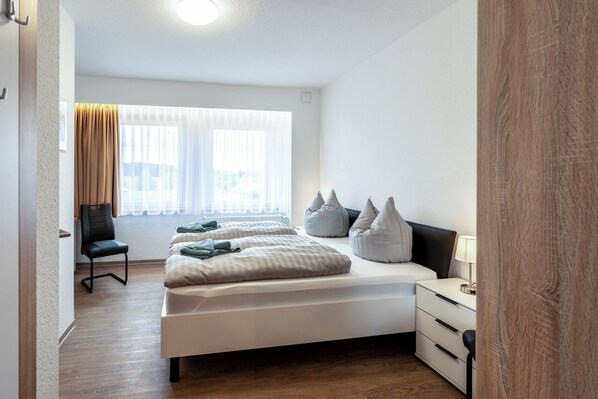A modern bedroom with a large bed, bedside tables, a chair, and a window with curtains. - Resort Dreistern - DZ 05, DZ 05 - Pension Resort Dreistern (Göda)