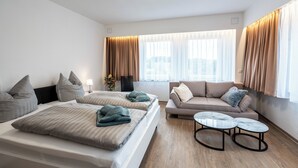 A modern hotel room with two beds, a sofa, a small table, and large windows with curtains. - Resort Dreistern - DZ 10, DZ 10 - Pension Resort Dreistern (Göda)