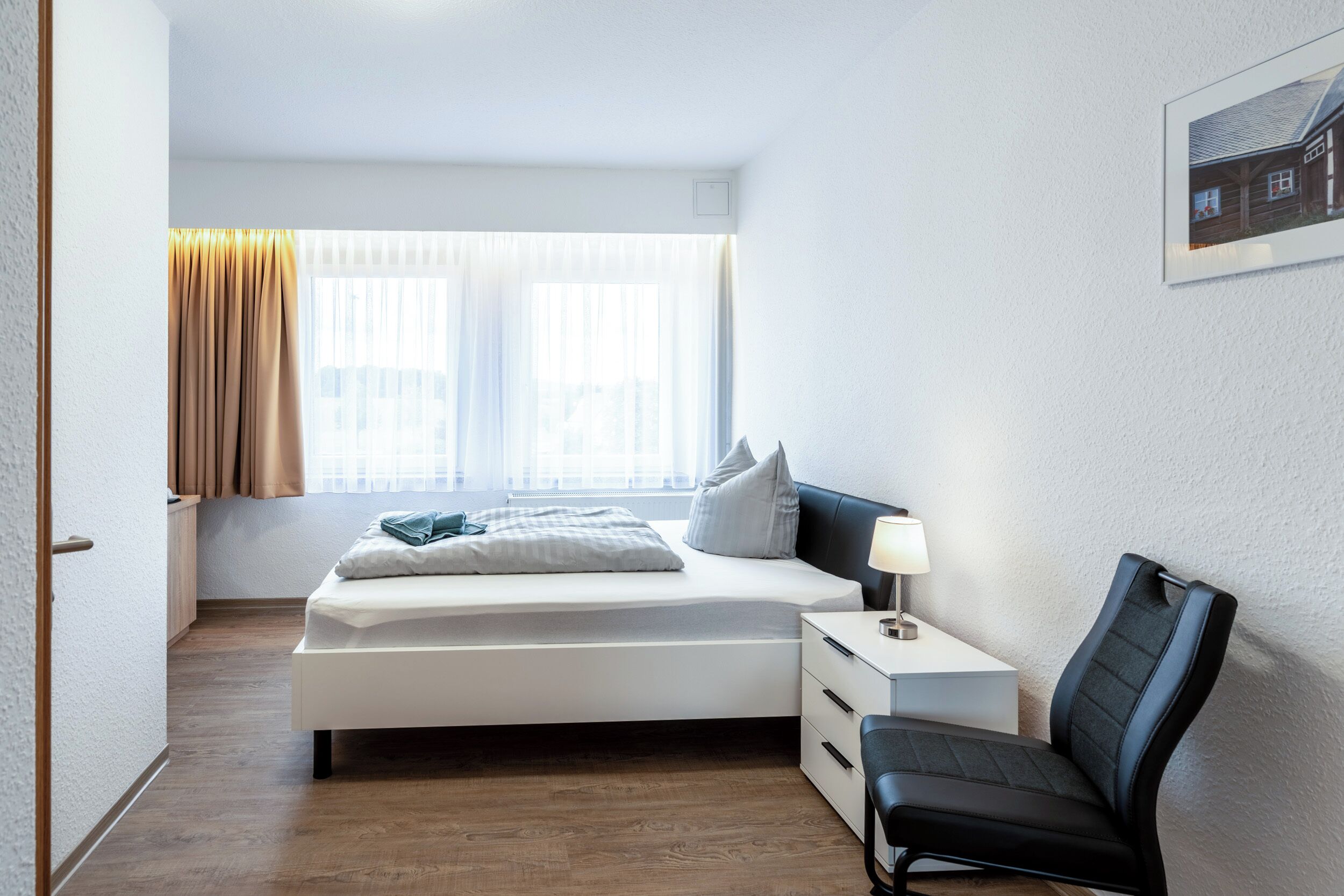 Ein Schlafzimmer mit Bett, Nachttisch, Stuhl und einem Fenster mit Vorhängen.