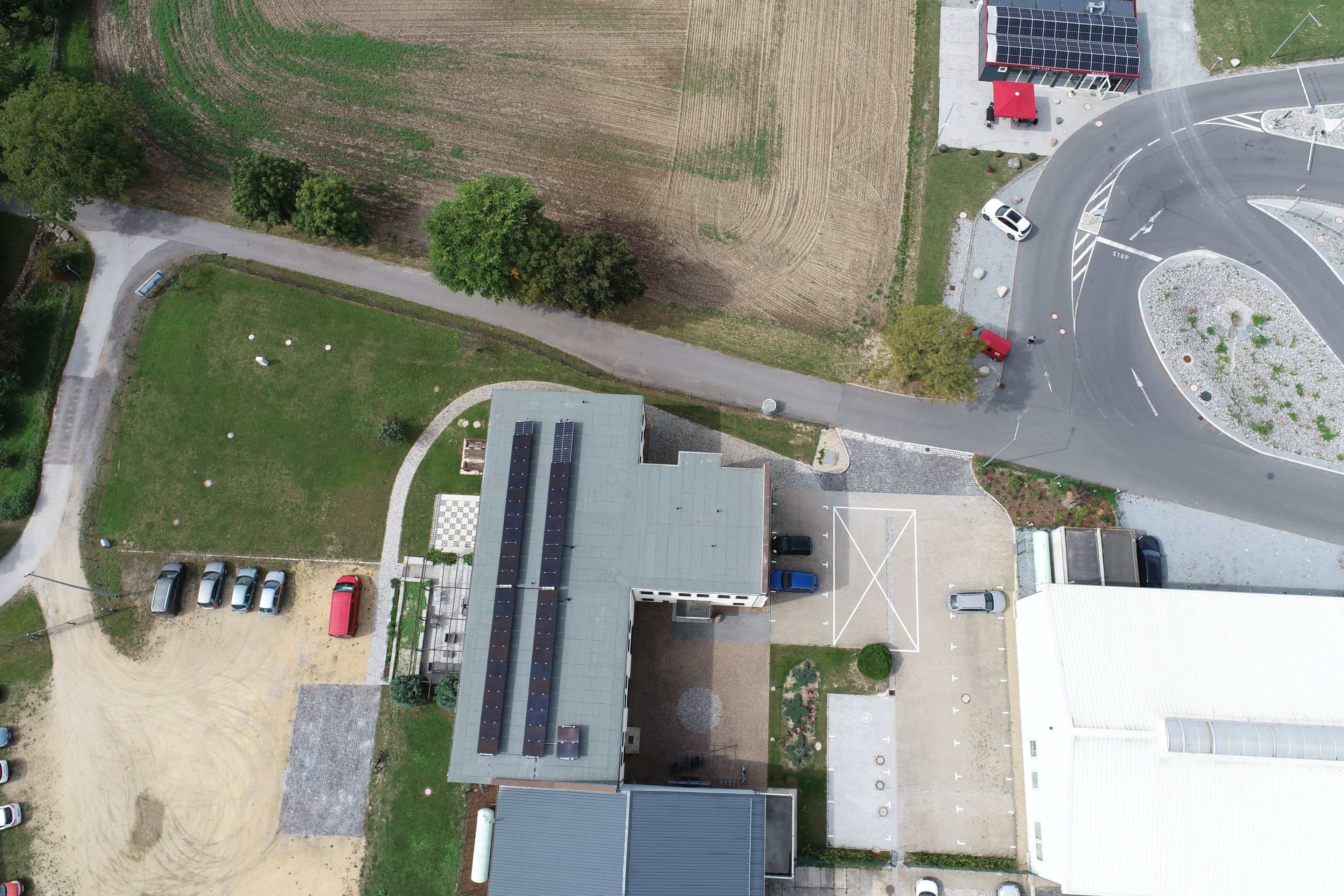 An aerial view of a building with a parking lot, solar panels, and a road intersection.