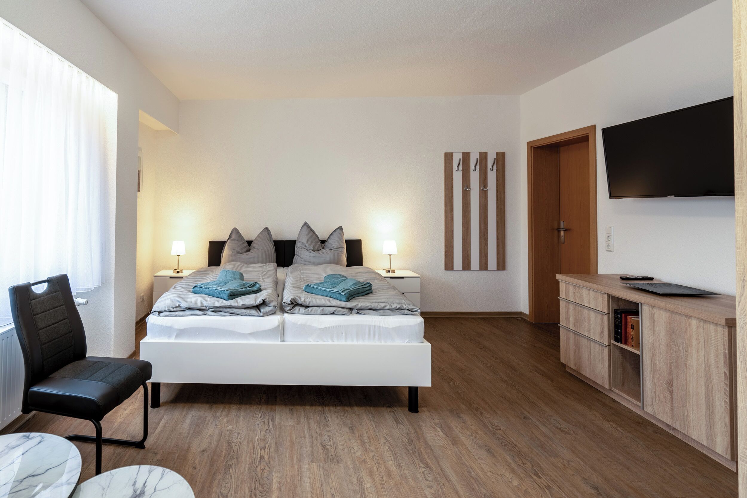 A modern bedroom with a large bed, bedside lamps, a TV, a wooden cabinet, and a chair.