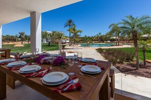 A dining table set outdoors with a view of a pool and palm trees.