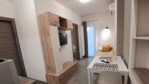 A modern, compact room with a wooden accent wall, a flat-screen TV, a dining table with chairs, and a bed with a yellow pillow. - Casa Belfiore - Martiri di Belfiore 23 (Vicenza)